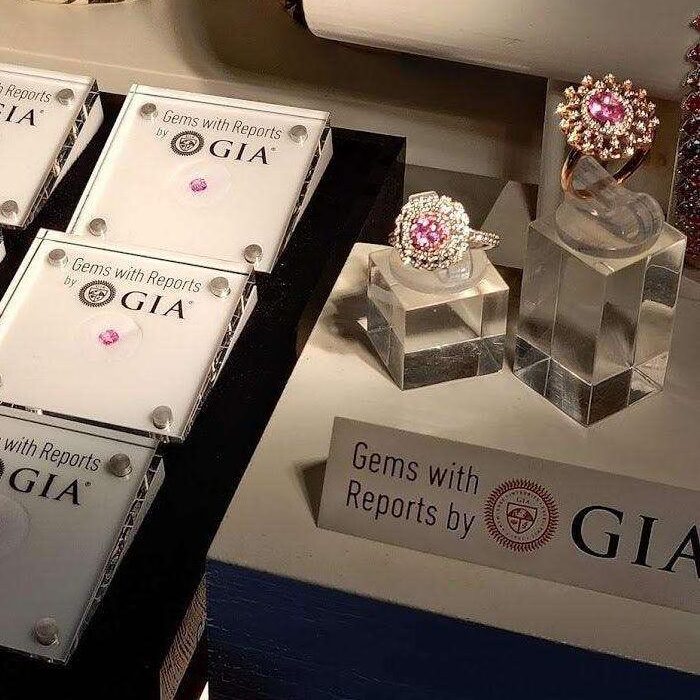 Forseglede ædelsten mærket Gems with Reports by GIA ved siden af to ringe på akrylstativer